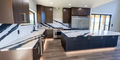 Modern kitchen with marble countertops and dark cabinets.