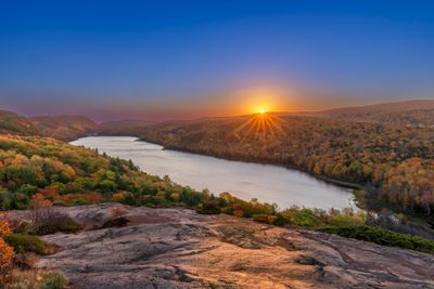 Sunset over a winding river surrounded by autumn foliage and rocky hills.