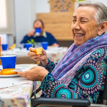 Elderly woman joyfully eating a pastry at a social gathering.