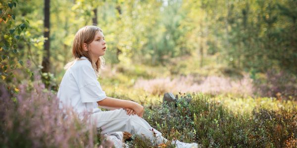 Child sitting thoughtfully in a forest clearing.