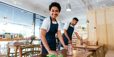 Two cafe workers cleaning tables with flowers in vases.