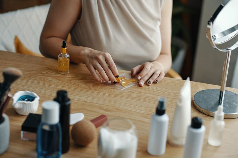 Person arranging various beauty products on wooden table in naturally lit room creating tidy workspace emphasizing skincare and self-care routine