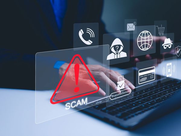 Person using laptop with scam warning and cybersecurity icons floating.