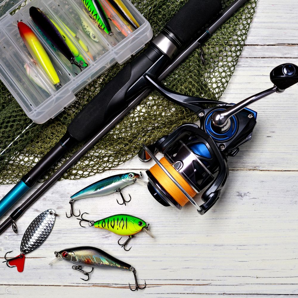 Fishing rod, reel, and colorful lures on a wooden surface.