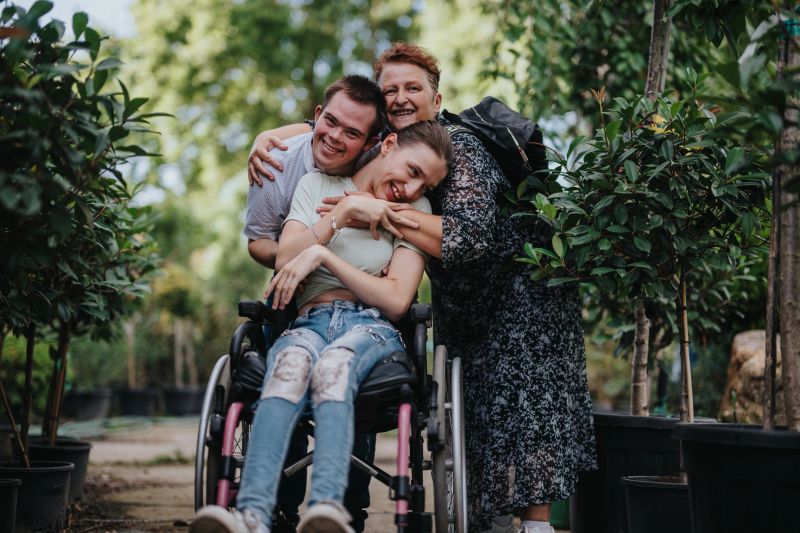 A group of friends, including a person in a wheelchair, share a joyful moment together in a lush garden. Their close bond and happiness are evident, highlighting inclusivity and friendship.