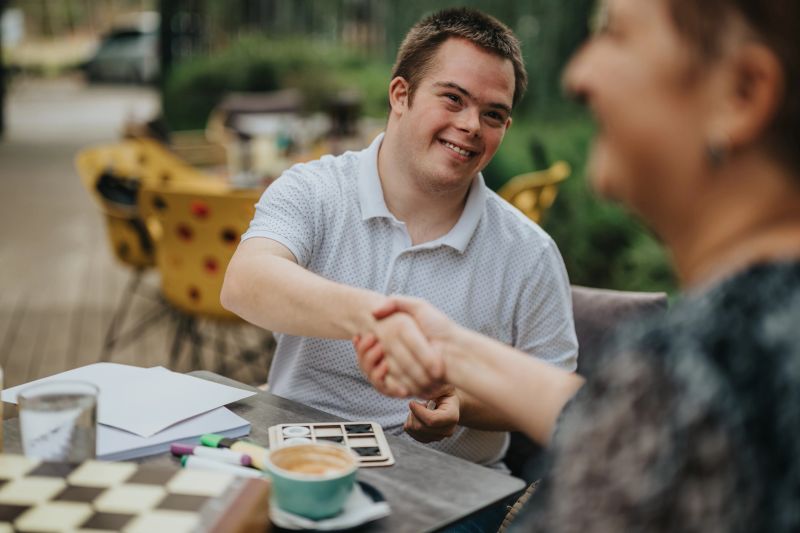 A lively gathering takes place at an outdoor café, where people enjoy their coffee and exchange handshakes, highlighting the warmth of friendship and the spirit of inclusivity.