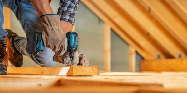 Worker using a cordless drill on wood in a construction setting.