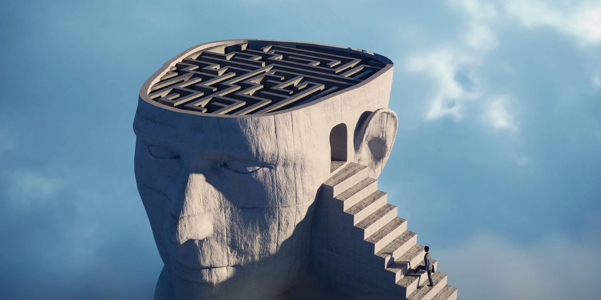 A person climbing stairs into a giant head with a maze inside.