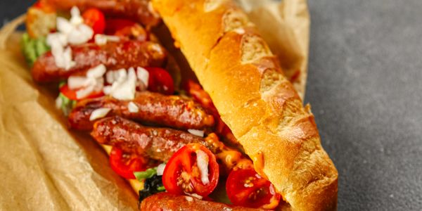 Delicious sausage sandwich with tomatoes and onions in a crusty baguette.