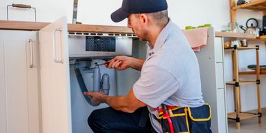 A plumber repairs a kitchen sink pipe using a wrench.