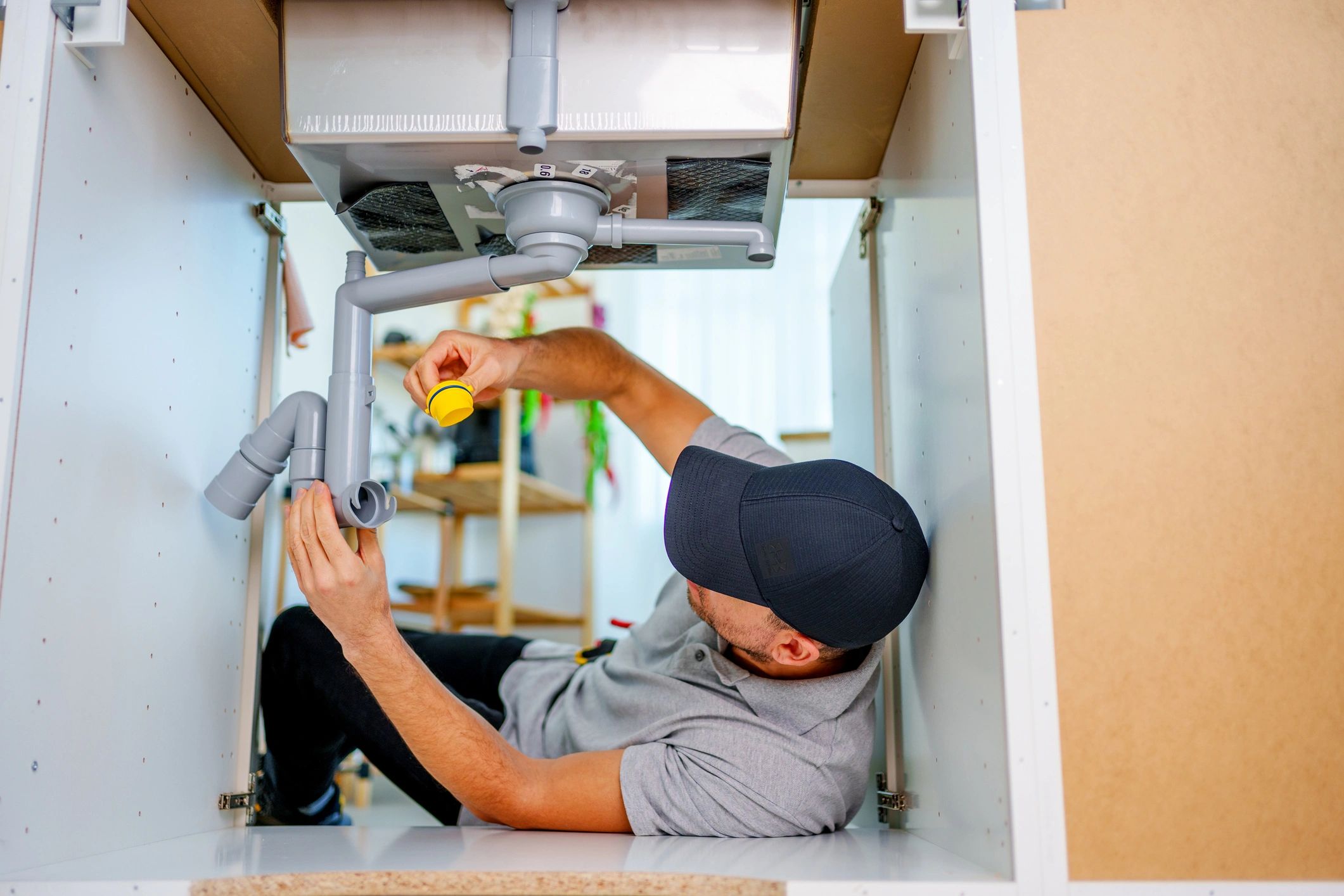 Plumber fixing sink pipes under a kitchen cabinet. Domestic plumbing 