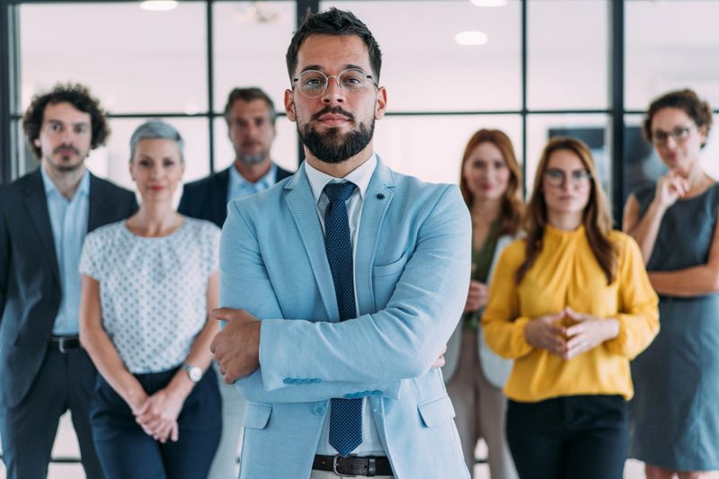 Portrait of handsome serious businessman with his colleagues. Group of business persons standing together in modern office. Successful team leader and his team behind him.