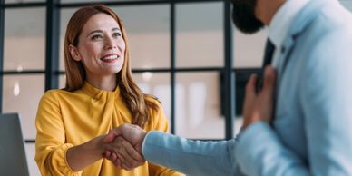 A woman in yellow shakes hands with a man in a suit in an office.