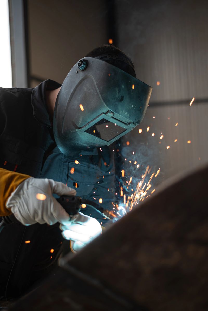 Welder wearing protective gear is joining metal parts together, creating a shower of bright sparks