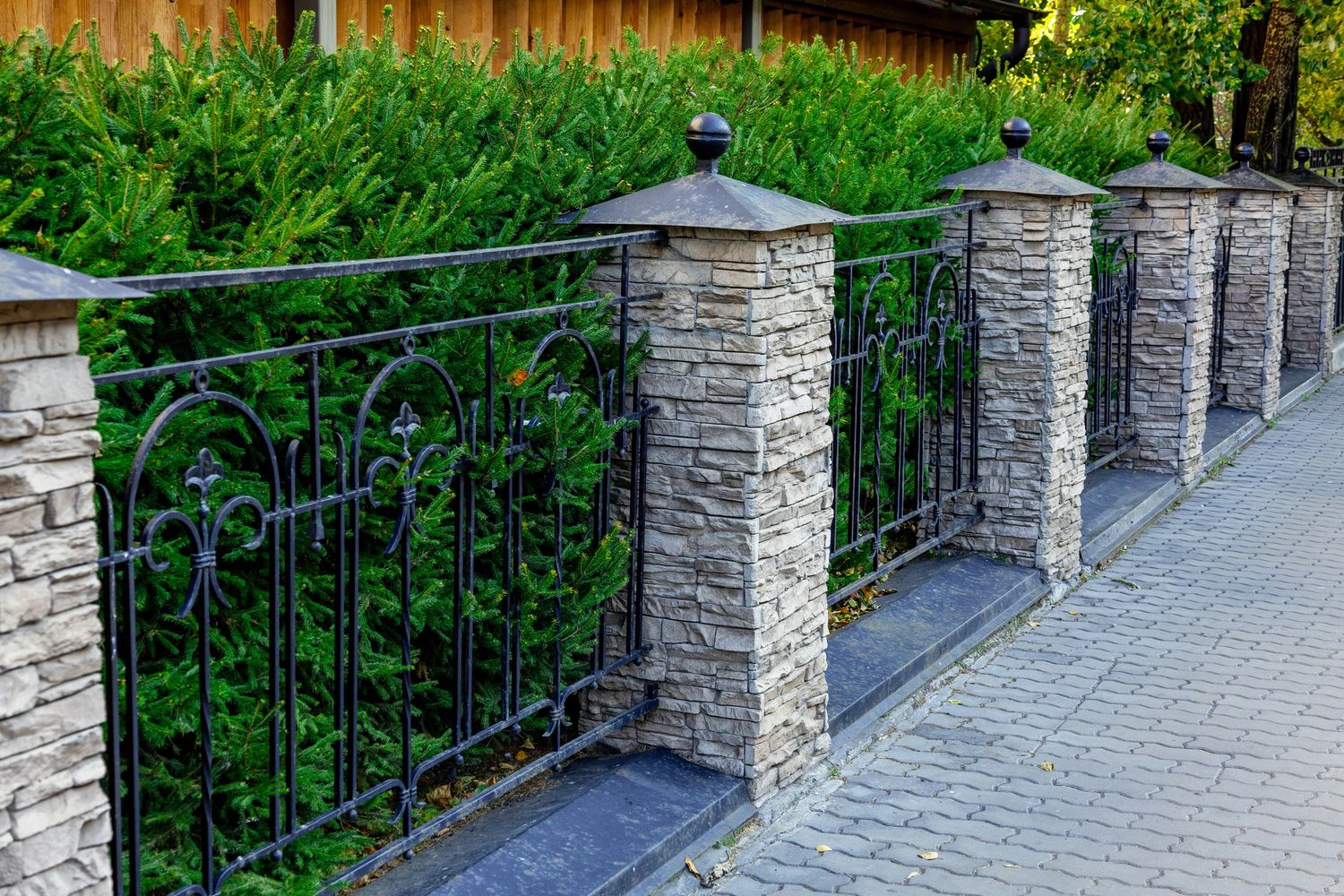 Stone pillars with wrought iron fence and lush greenery behind.