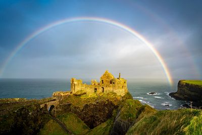 Ancient castle ruins under a vibrant rainbow by the sea.