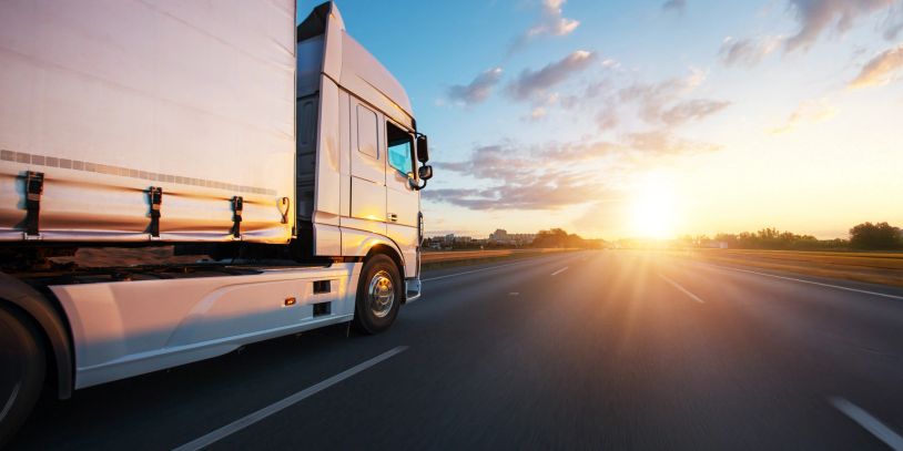 A white truck drives on an empty highway at sunset.
