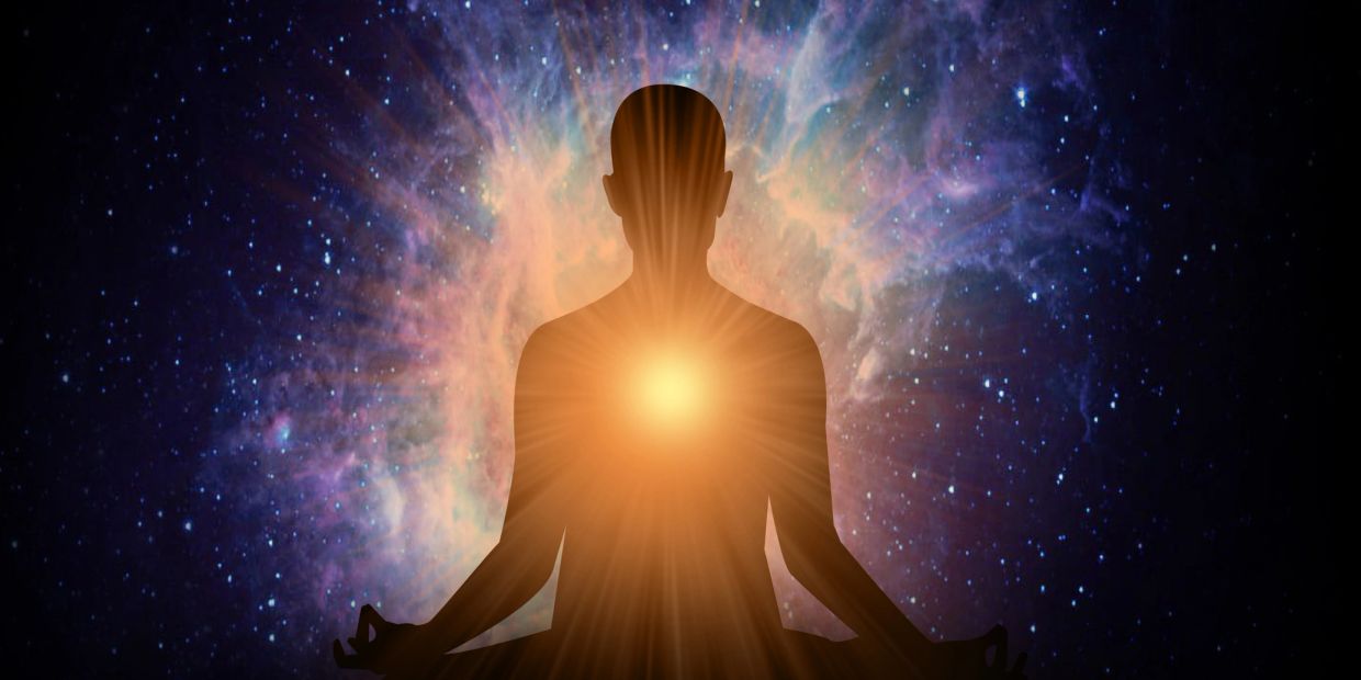 Silhouette meditating with glowing light in chest against cosmic background.