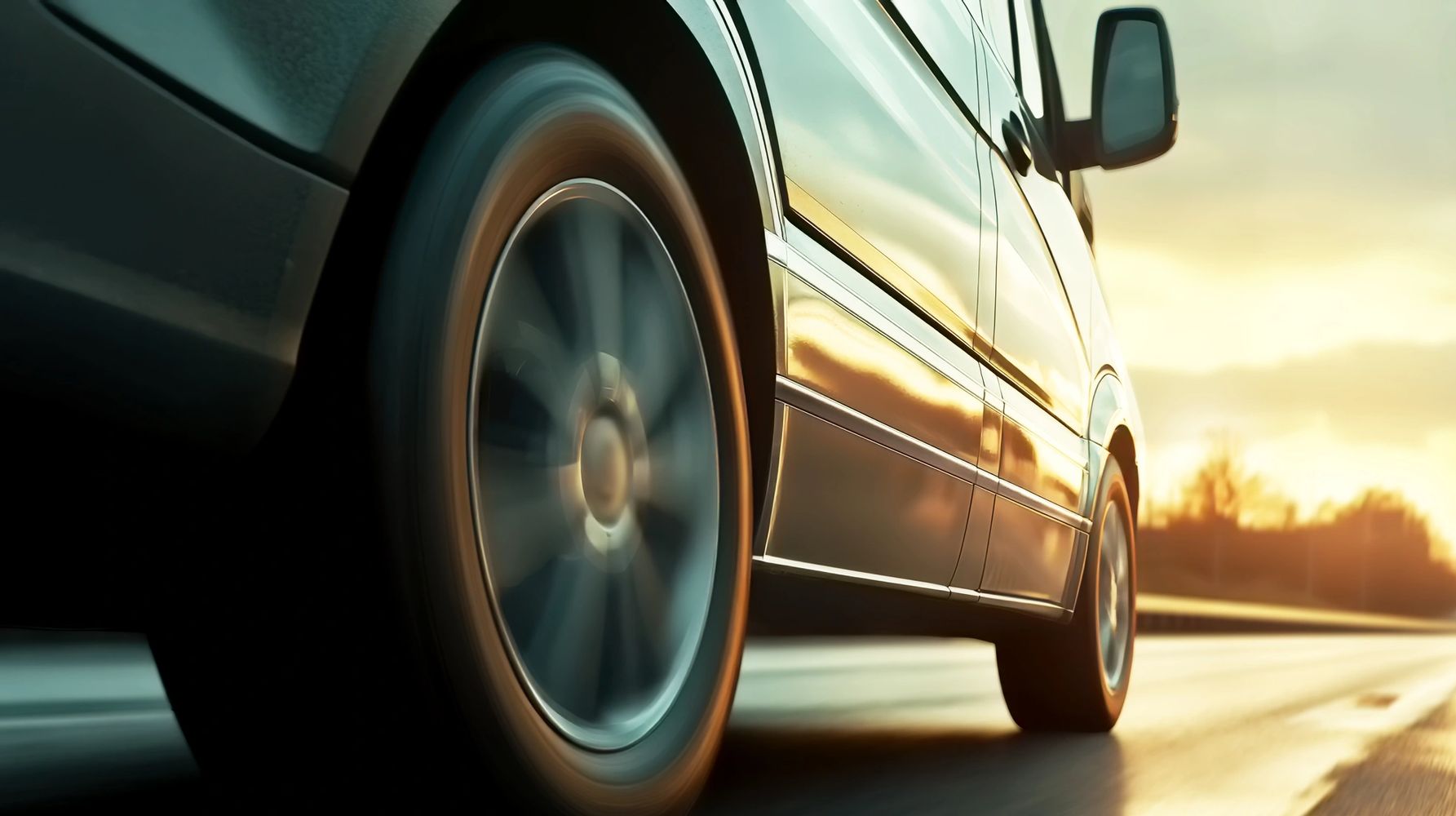 A car is driving down the street at sunset.