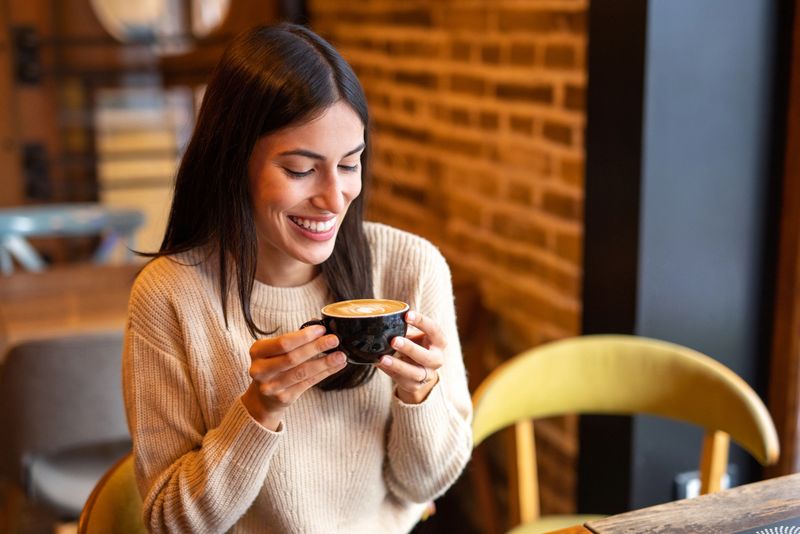 Happiness can often be found in the little things. Smiling woman enjoying coffee in cafeteria, holding coffee cup and looking at foam decoration, ready to take a sip.
