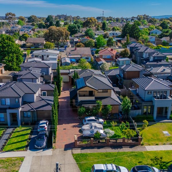 Aerial view of a suburban neighborhood with houses and greenery under a clear blue sky.