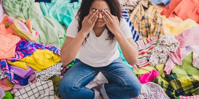 Woman overwhelmed by a large pile of colorful clothes around her.