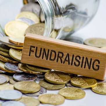 Coins spilling from a jar with a wooden block labeled 'FUNDRAISING'.