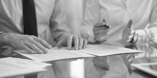 Two professionals reviewing and discussing documents at a glass desk.