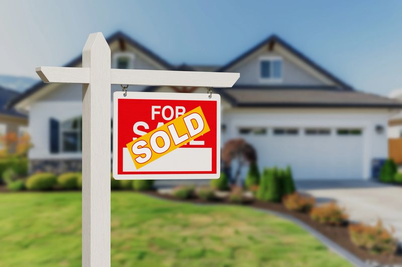 Real Estate Wooden Sign with Yellow Sold Sticker is Displayed in Front of a House with a Blurred Background. 3d Rendering