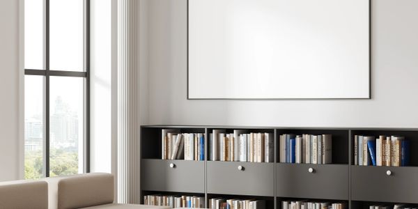 Modern living room with beige sectional sofa, marble coffee table, and built-in bookshelf under a blank wall frame.