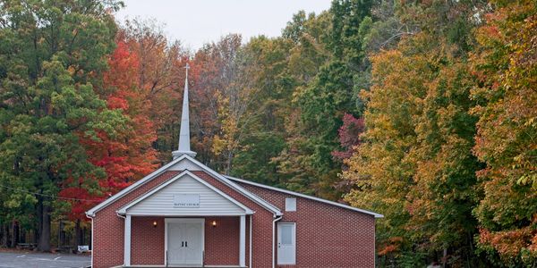 Small brick Baptist church surrounded by autumn trees.