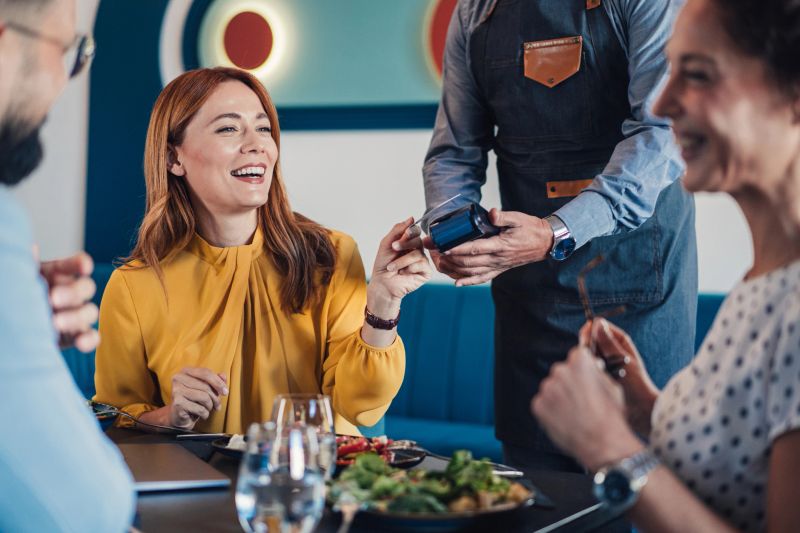 Shot of a businesswoman paying for a lunch with business entrepreneurs. Group of businesspeople enjoying lunch at a restaurant, and businesswoman paying with a credit card via contactless payment. Business people paying the restaurant check using contactless payments after a meeting. Businesswoman making payment in cafe through credit card. Customer paying bill of lunch with debit card. Woman paying for a lunch with business colleagues.