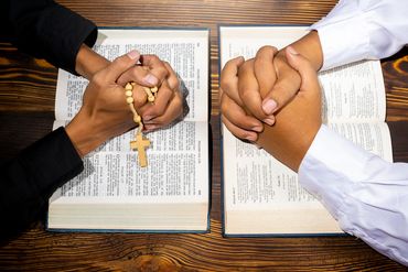 Two people praying with Bibles and a rosary.