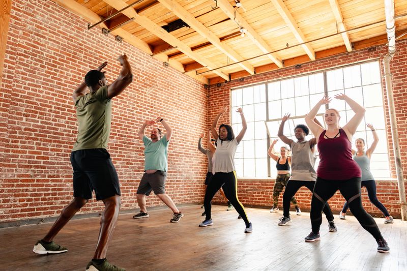 Group fitness class with diverse participants in a studio. People of various ethnicities and genders engaged in exercise. Energetic workout session. Diverse people exercising in fitness class.