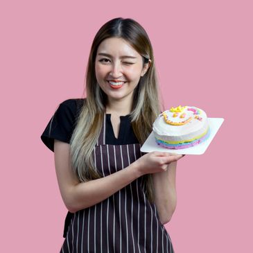 Smiling woman winking while holding a colorful cake against a pink background.