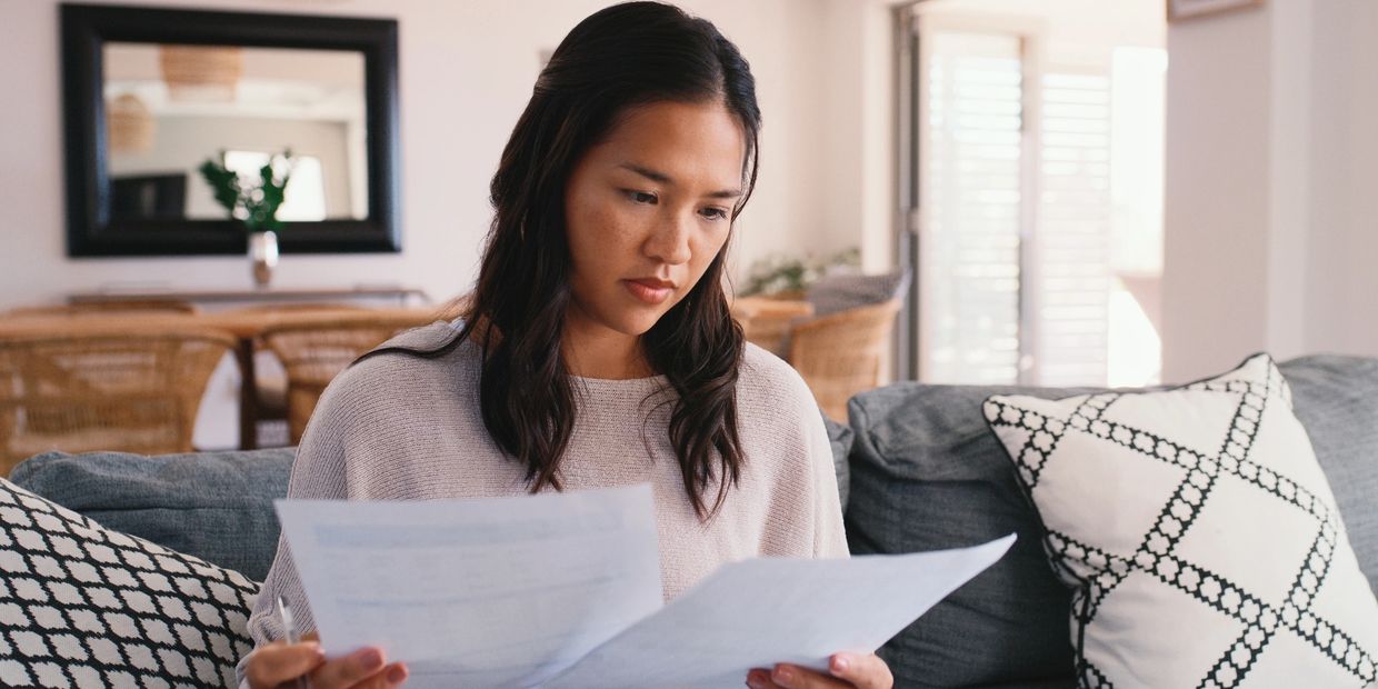 A woman intently reviewing documents on a couch in a cozy living room.
