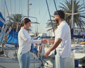 Two people shaking hands at a marina with boats in the background.