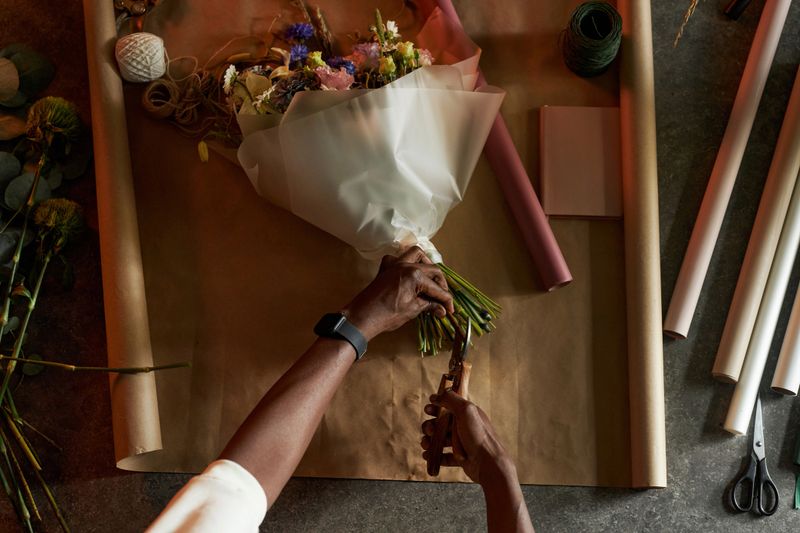 Minimal top view of male hands finishing details of beautiful flower bouquet on table with craft paper background copy space