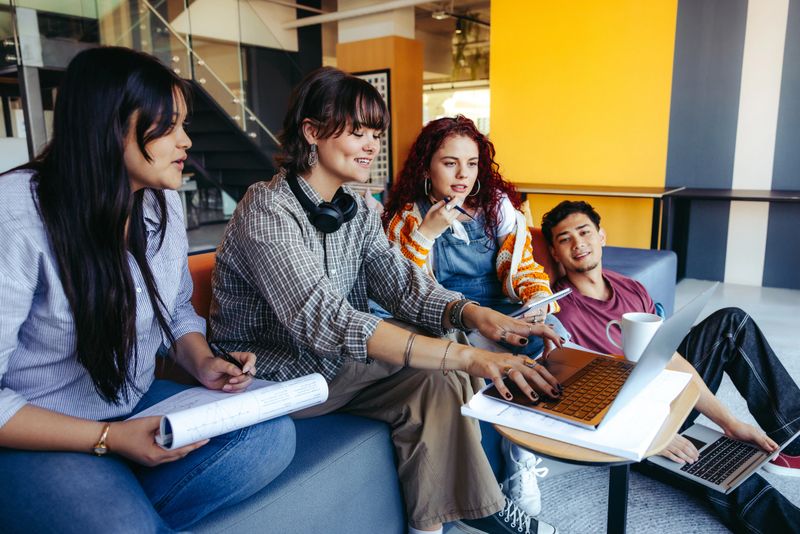A casual group of young adults engages in a collaborative project using laptops in a contemporary office, emphasizing teamwork and creativity.