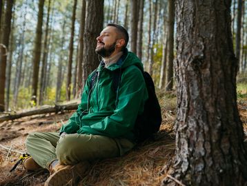 Man in green jacket meditating in the forest.