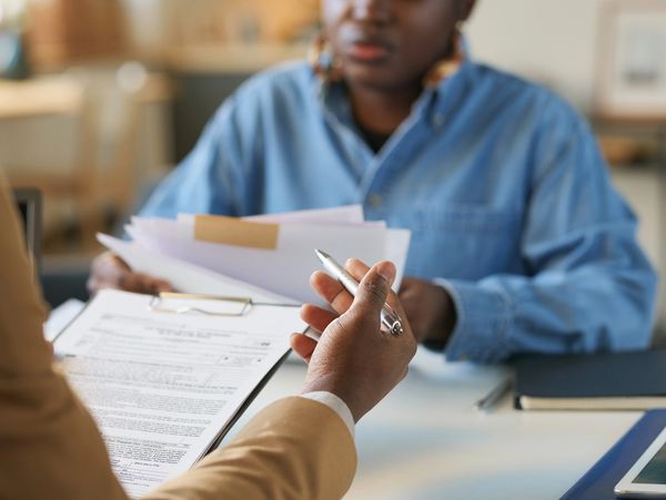 Two people discussing documents at a desk in a professional setting.