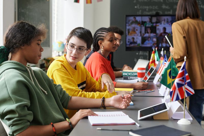 Multiethnic group of students sitting at table with country flags and communicating during international conference, copy space