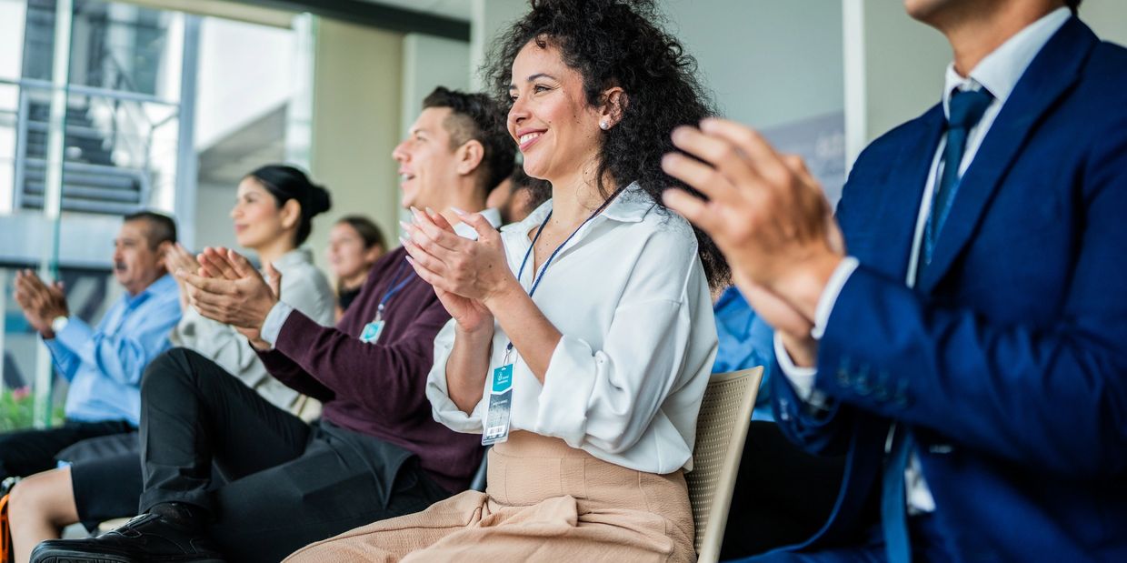 A diverse group of professionals clapping and smiling in a conference room.