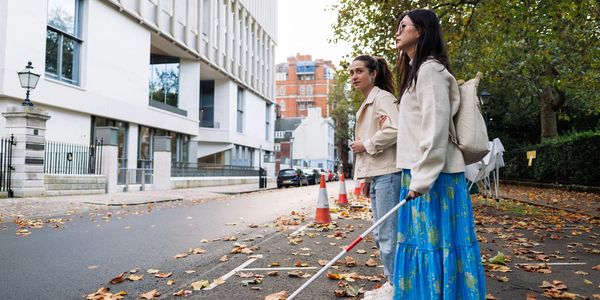 A blind person being guided, while waiting to cross the road.