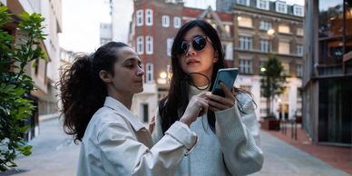 Image of two women using a GPS app on their phone to navigate using a white cane in a city