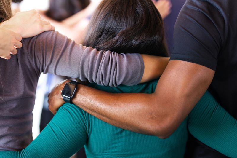 Group of diverse people with arms around hugging each other, showing unity and support. Close-up of hugging arms and shoulders, emphasizing connection and togetherness.