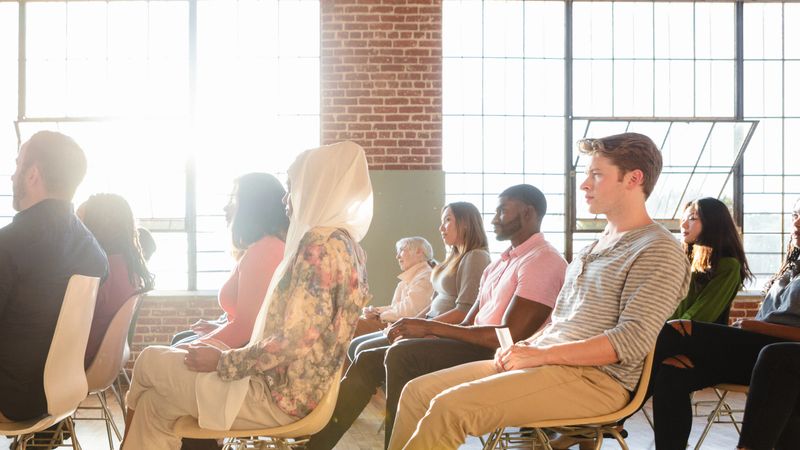 Diverse group of people attend business seminar in bright room. Business seminar audience sit and listen to presentation. Seminar room with diverse audience group of people, business presentation