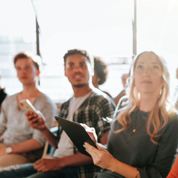 Diverse group attentively listening with digital devices in a bright meeting room.