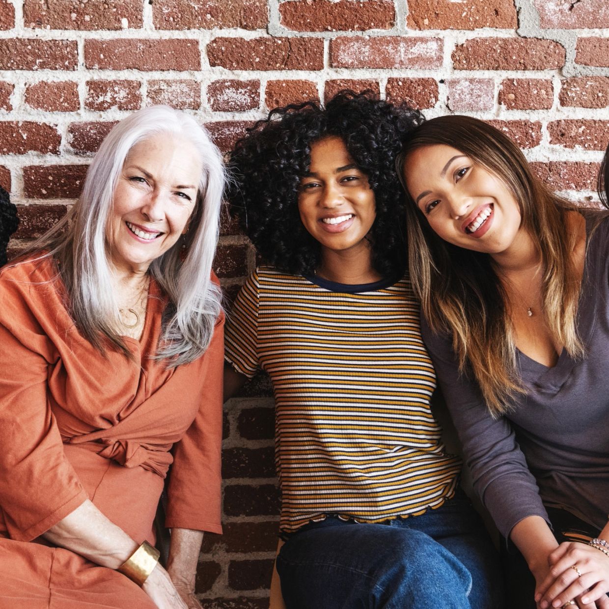 Three diverse women smiling against a brick wall.
