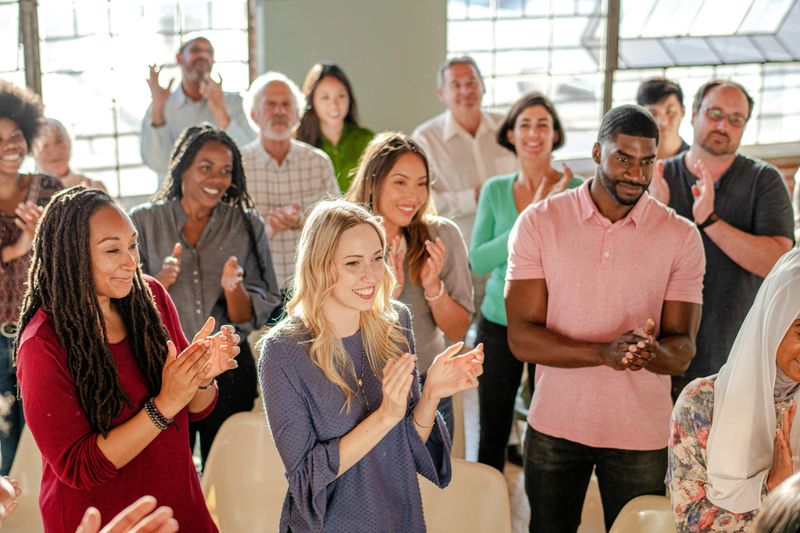 Diverse group of people applaud in social meeting, smiling and clapping. Diverse group of smiling men and women applauding, clapping in social gathering. Diverse audience group clapping, happy people